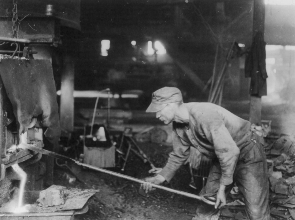 A puddler draining cinder from a puddling furnace after the extraction of the balls of molten iron (circa 1919).